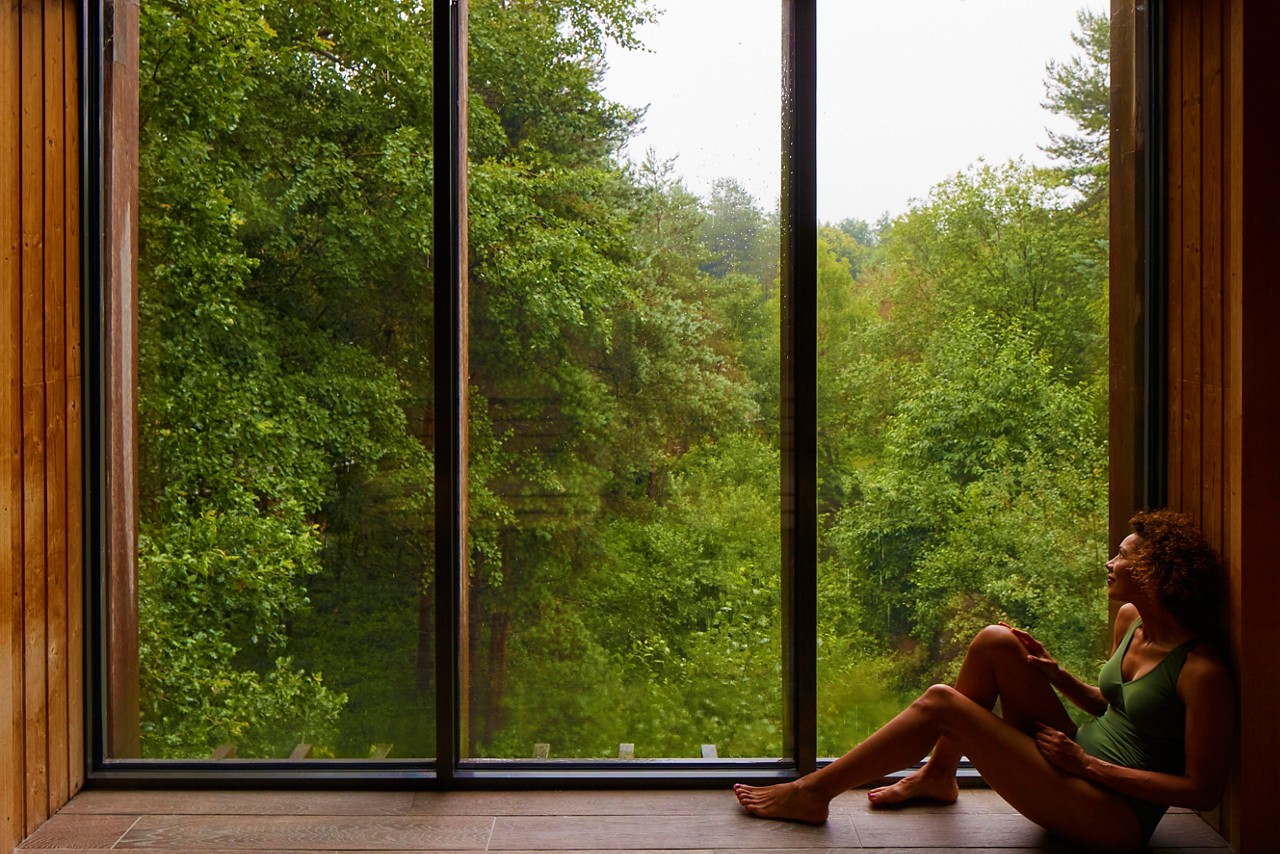 Woman sat looking out at the forest from inside the Treetop Sauna.